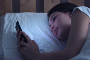 ragazza a letto con cellulare in mano