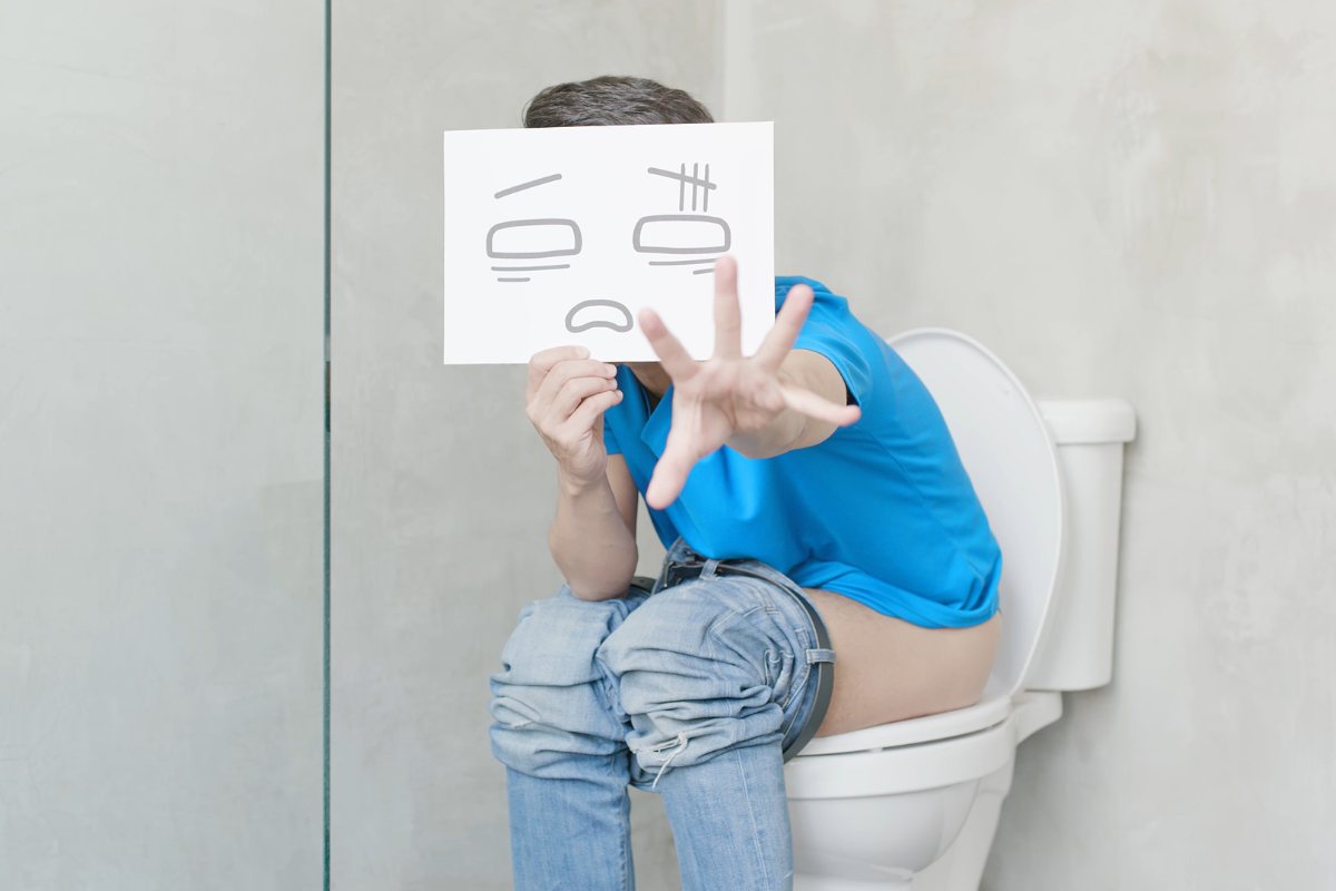 Persona seduta sul water con il cartello di uno smile sofferente disegnato in faccia e la mano tesa