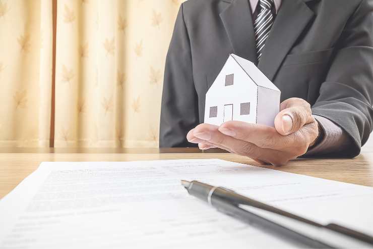 scrivania con foglio e penna, casa in miniatura in mano