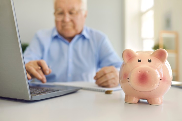 Pensionato al pc sullo sfondo e salvadanaio in primo piano