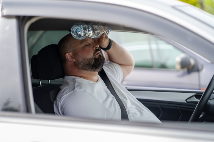 uomo che ha caldo in auto con bottiglia acqua in fronte